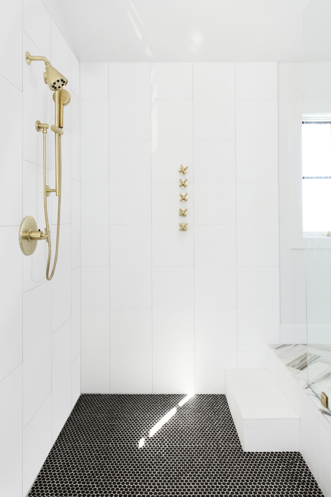 a white bathroom with a gold shower head and black floor.