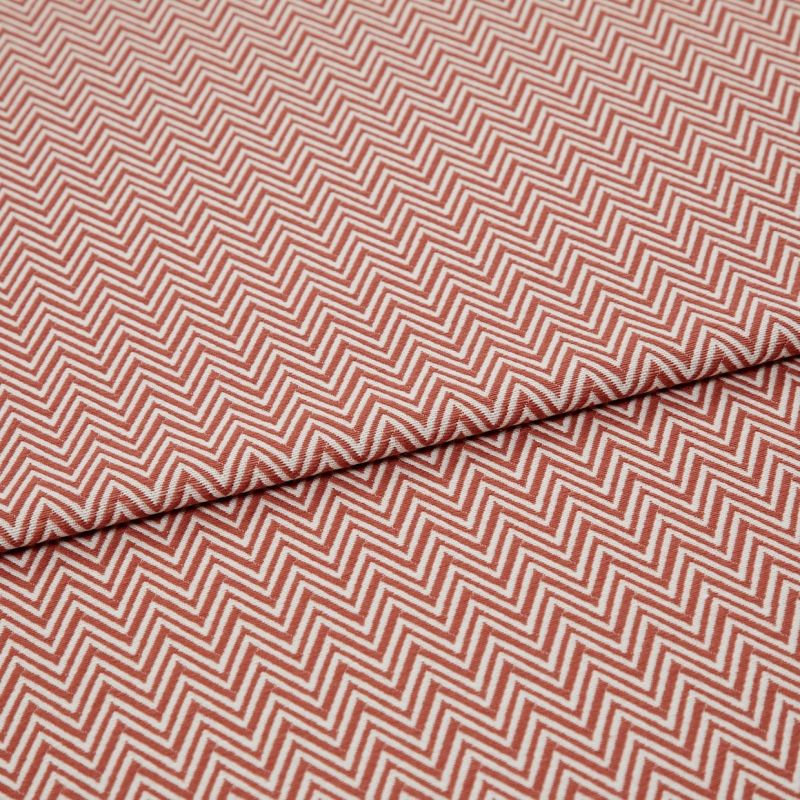 Chevron-patterned textile (red and white) folded across the frame, showing tight zigzag lines; fabric lies flat with a single fold, photographed in even studio lighting on a neutral background.