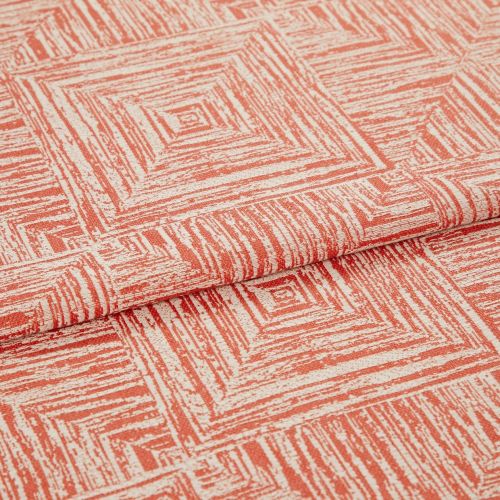 Folded coral-and-cream fabric with textured concentric-square print; a layered fold reveals repeating pattern, shown close-up on a flat surface under soft, even lighting.