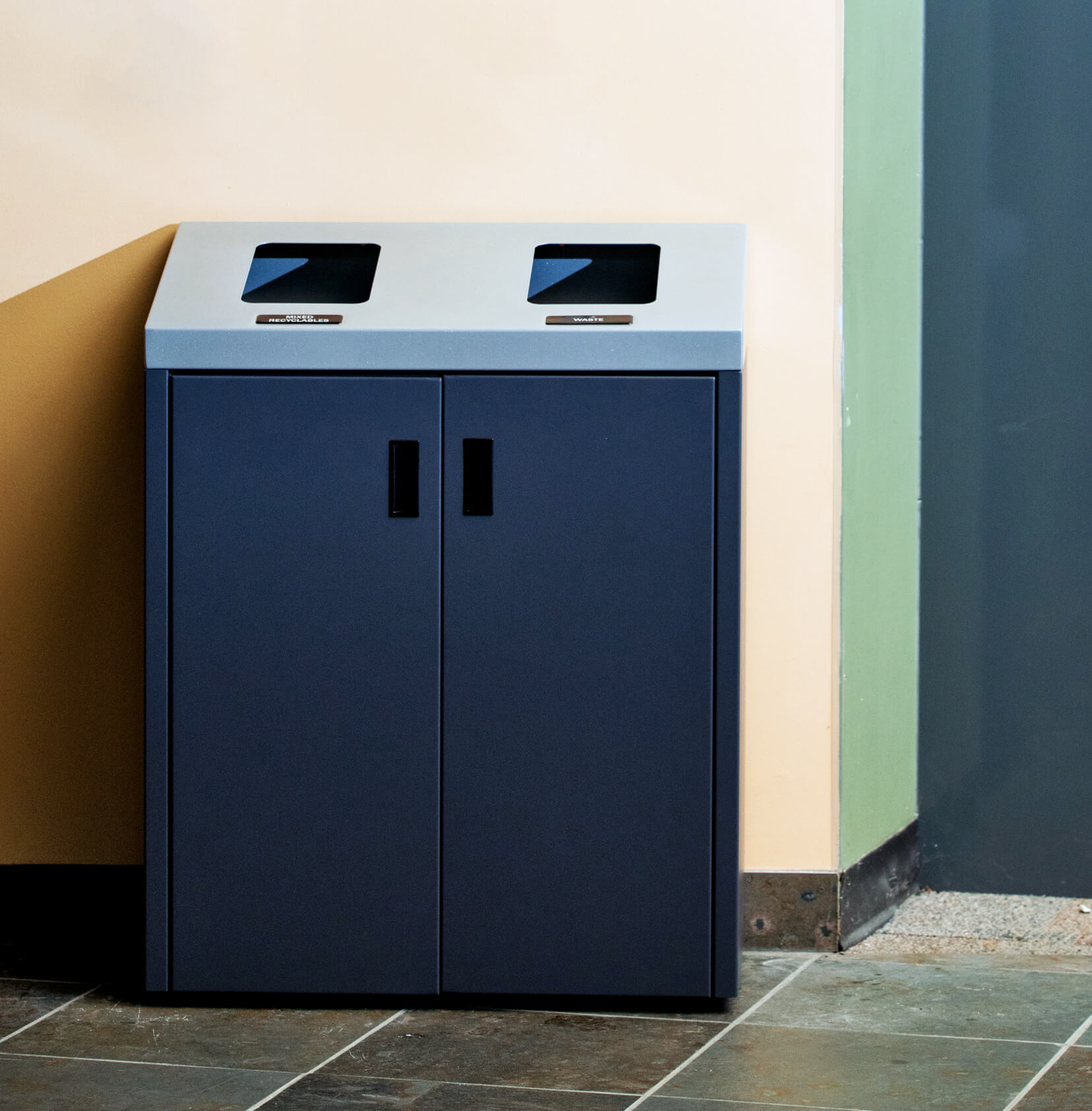 metal recycling and waste container with sloped lid and front doors in a corporate office