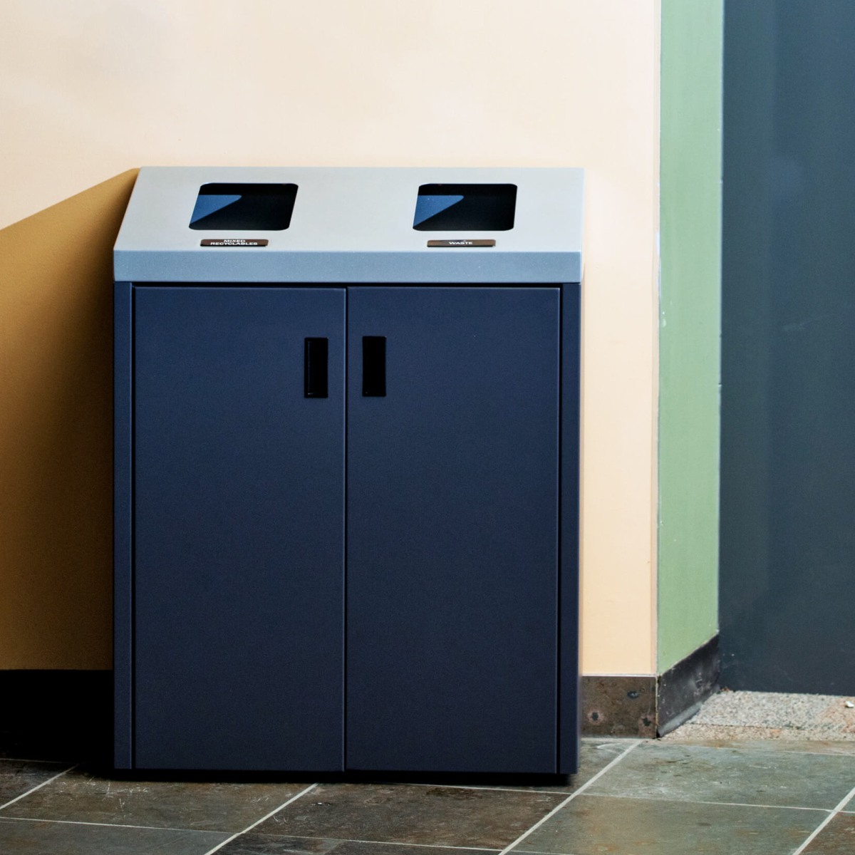 metal recycling and waste container with sloped lid and front doors in a corporate office