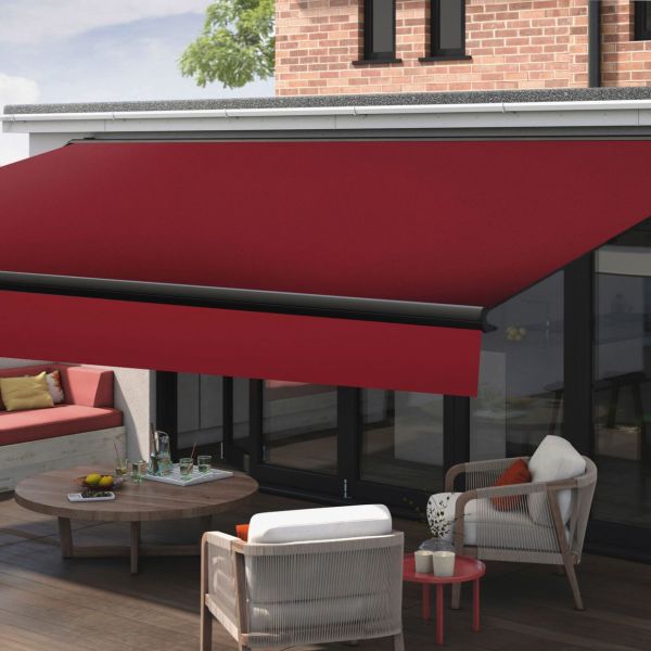 Red retractable awning with black support bar mounted above sliding glass doors, fully extended and shading an outdoor patio seating area with wooden table, chairs and brick façade in daylight.