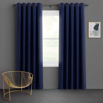 Navy grommet-top blackout curtains, two panels hung on a metal rod, parted slightly to reveal a bright single-pane window; minimalist living space with gray walls, gold wire chair, soft daylight.