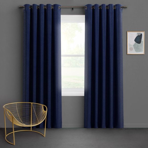 Navy grommet-top blackout curtains, two panels hung on a metal rod, parted slightly to reveal a bright single-pane window; minimalist living space with gray walls, gold wire chair, soft daylight.
