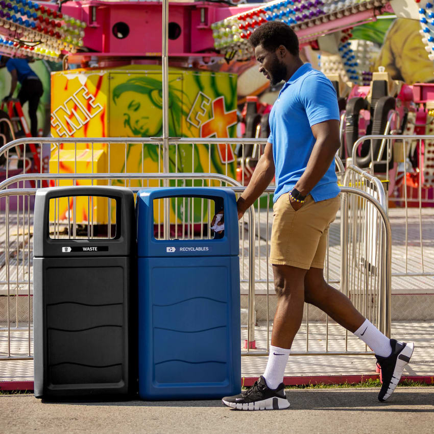 double waste and recycling containers made from 100% post-consumer recycled material outside at a fall fair with a man walking by putting recycling in the bin