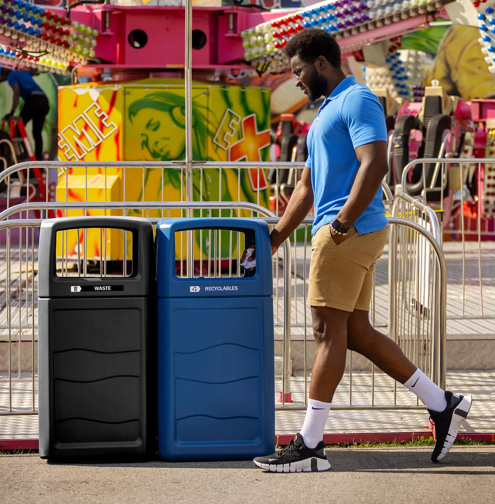 double waste and recycling containers made from 100% post-consumer recycled material outside at a fall fair with a man walking by putting recycling in the bin