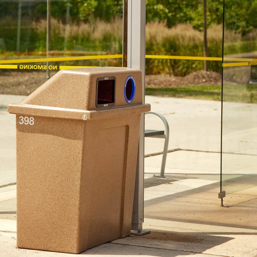 durable LDPE plastic waste and recycling container with hinged lid placed beside a transit shelter on a municipal sidewalk