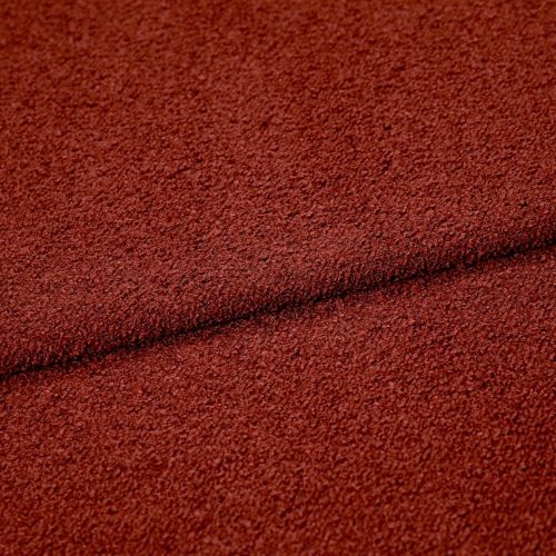 Rust-red textured boucle fabric folded across the frame, creating a dark seam; close-up studio view highlighting coarse looped surface and even, warm lighting.