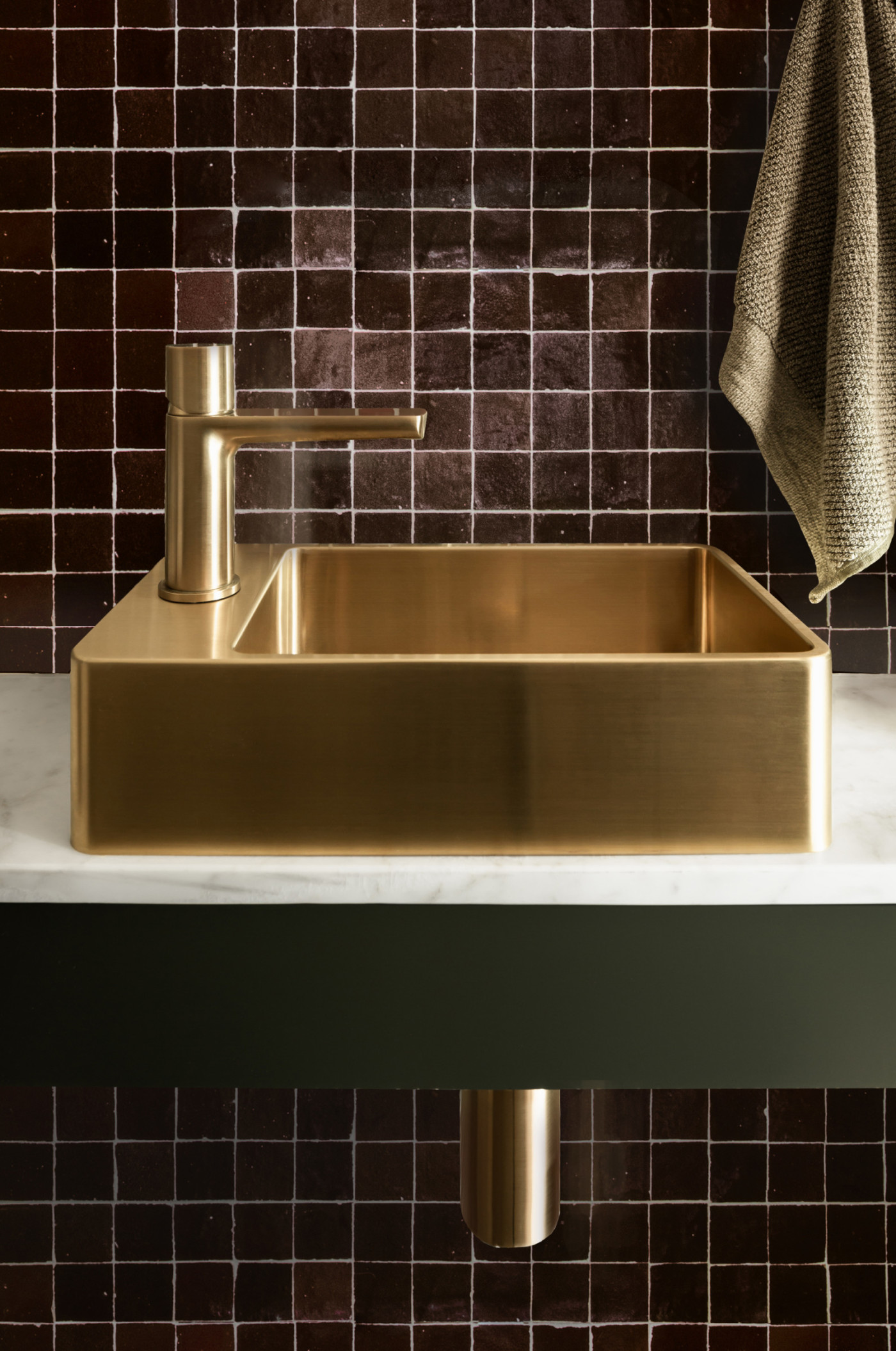 a gold sink in a bathroom with a brown tiled wall.