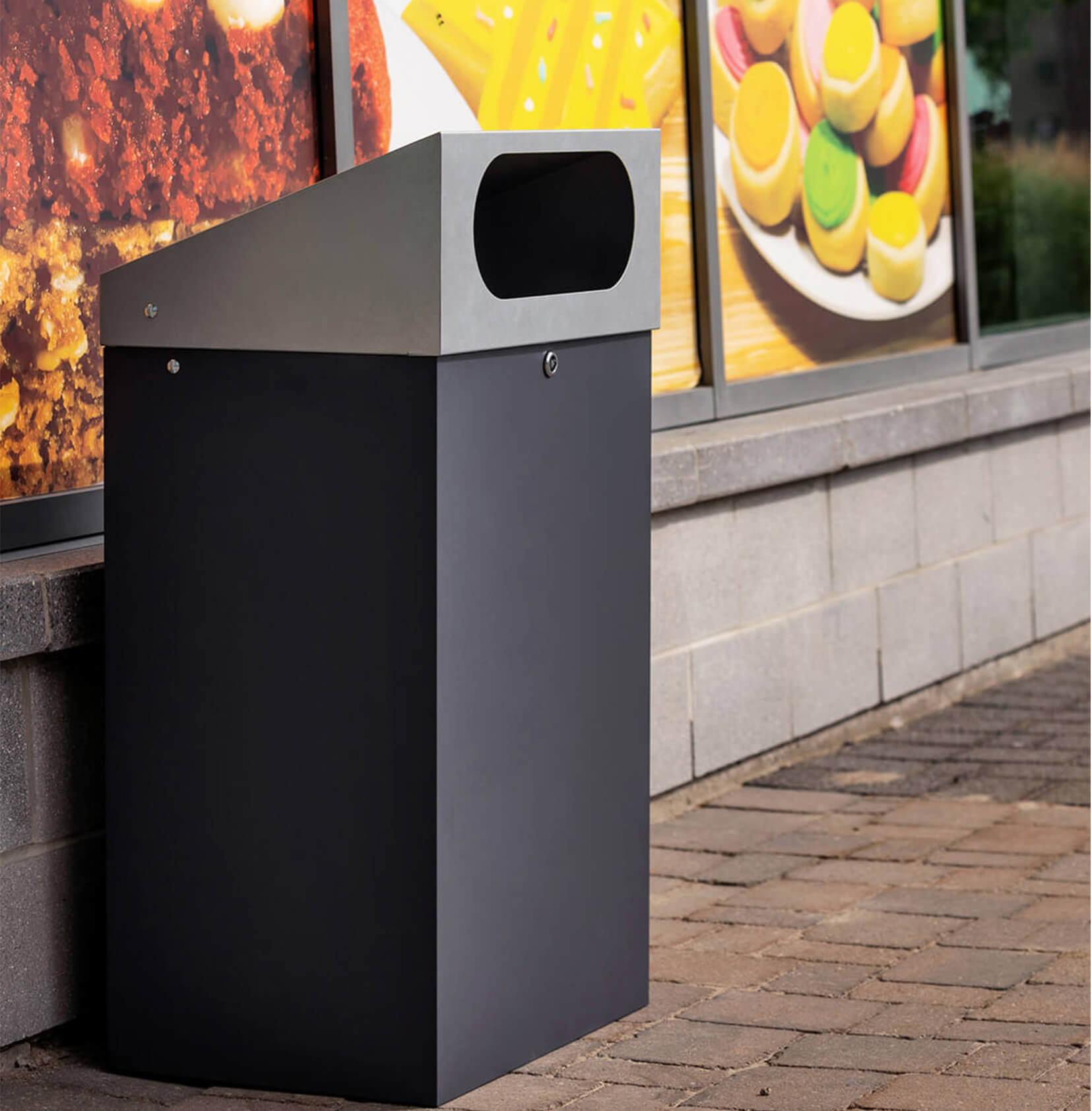 durable powder coated steel outdoor trash bin with locking lid and large waste opening outside a shopping plaza