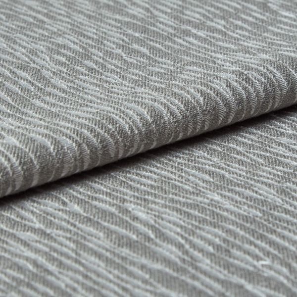 Folded grey woven fabric with raised, wavy ribbed texture (object) layered across itself (action) in a close-up, neutral-lit studio view emphasizing tactile detail (context).