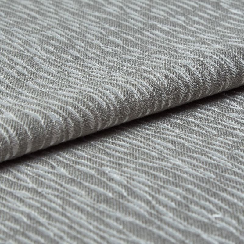 Folded grey woven fabric with raised, wavy ribbed texture (object) layered across itself (action) in a close-up, neutral-lit studio view emphasizing tactile detail (context).