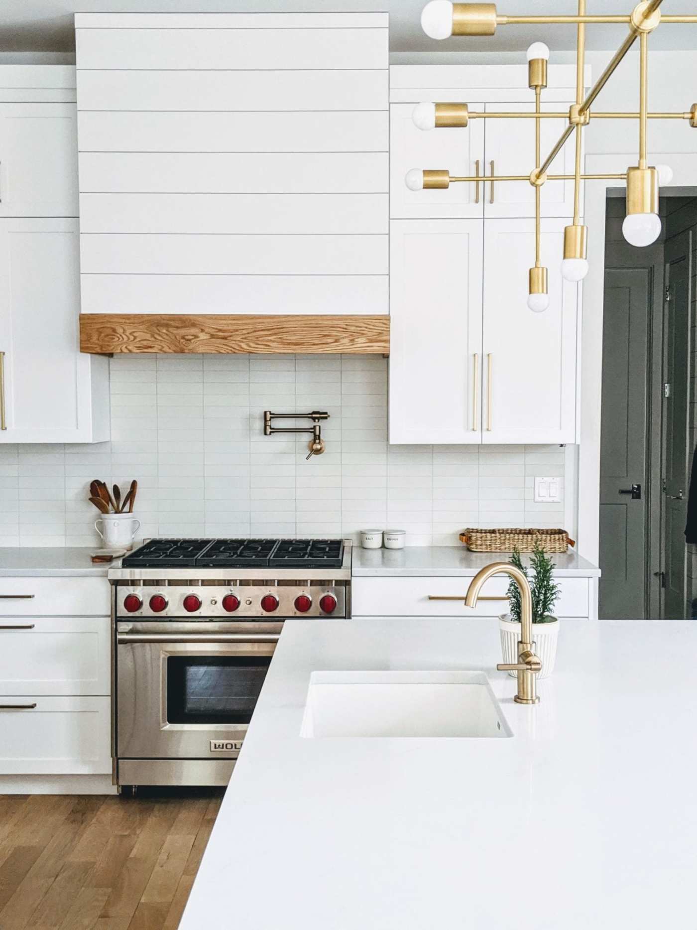 a white kitchen with wooden cabinets and a gold pendant light.