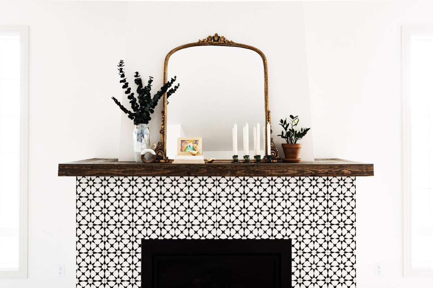 a black and white fireplace mantel with a mirror and potted plants.