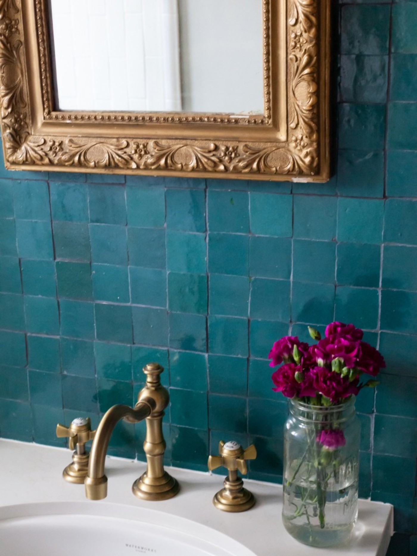 a bathroom with green tiles and a gold mirror.