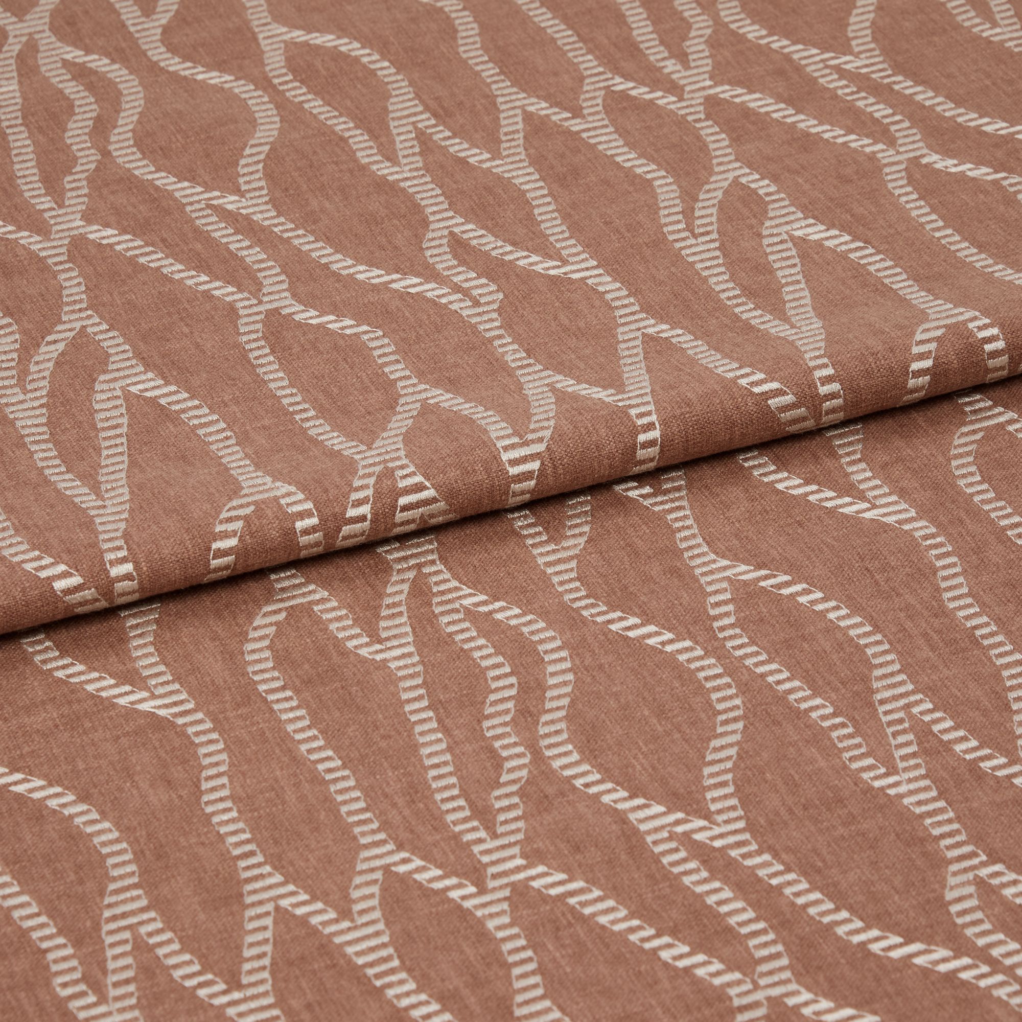 Folded terracotta-brown fabric with raised white embroidered undulating chain pattern, folded over itself with a horizontal overlap, close-up studio view emphasizing woven texture and soft, even lighting.