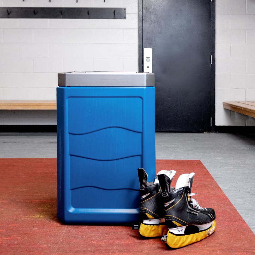 blue plastic recycling container with a brushed pewter plastic lid inside a hockey change room with a pair of skates on the floor beside the bin