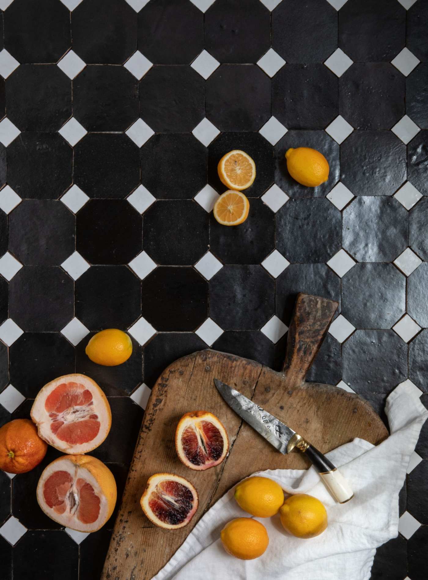 a cutting board with oranges and lemons on it on a black and white tile counter.