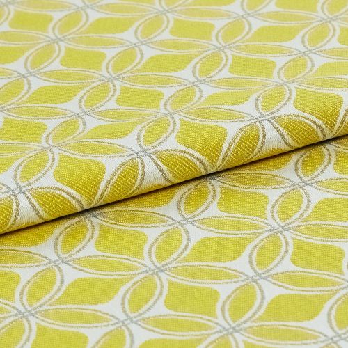 Folded yellow-green jacquard fabric with cream embroidered interlocking petal motif, close-up on a flat surface with bright even lighting, presented as a textile sample for upholstery or curtains.