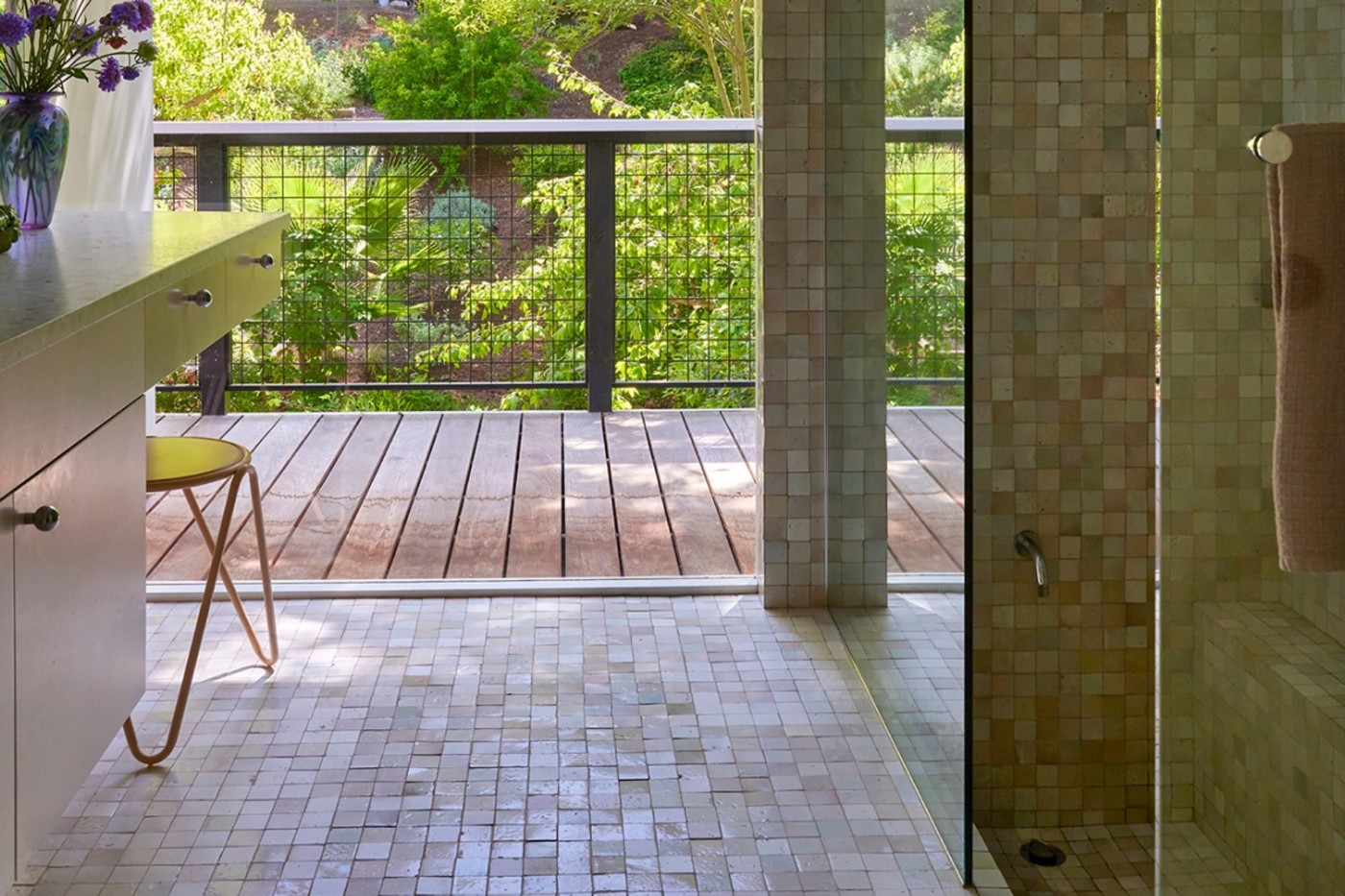 a tiled bathroom with a glass shower and large windows leading to a porch.