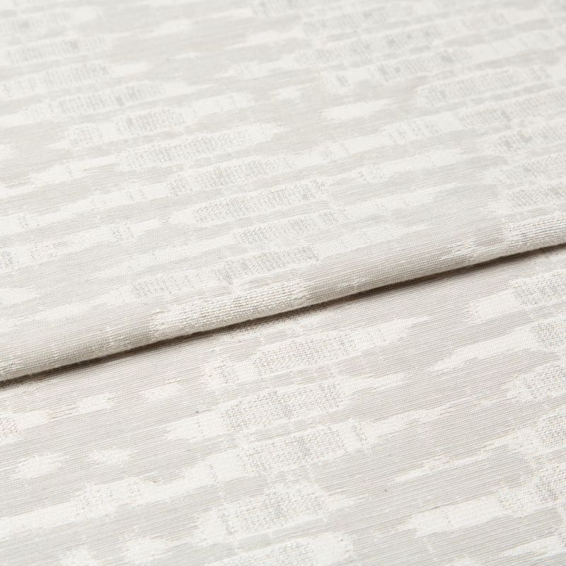 Off-white woven curtain fabric folded horizontally, showing a subtle geometric jacquard pattern; soft, diffused light highlights the texture in a neutral, close-up interior view.