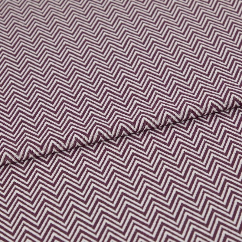 Folded fabric featuring tight purple-and-white chevron stripes, folded to form a shallow diagonal ridge; close-up view of a flat textile sample with even, neutral lighting.