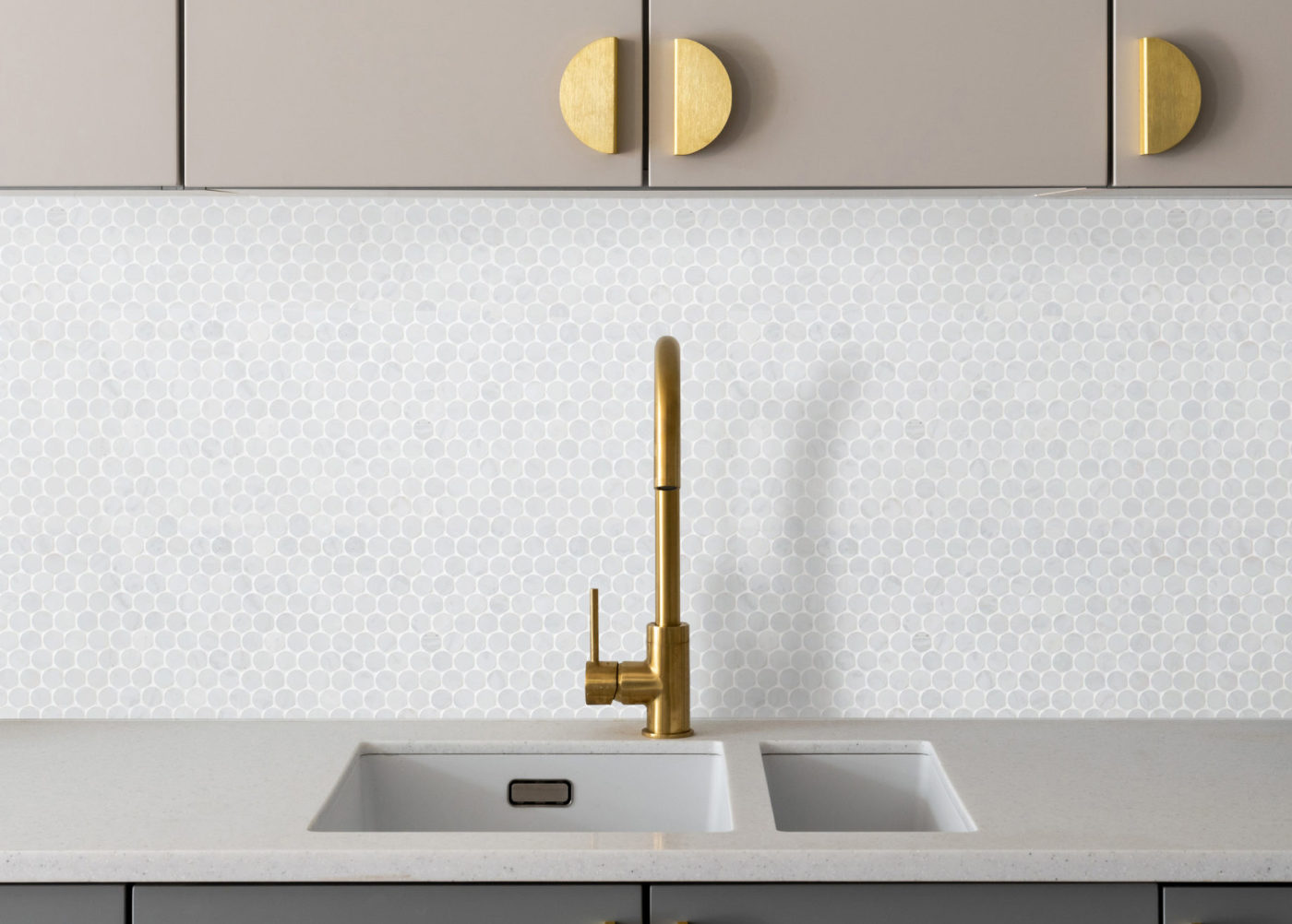 a kitchen with a sink, marble colored tile backsplash, and gold handles.