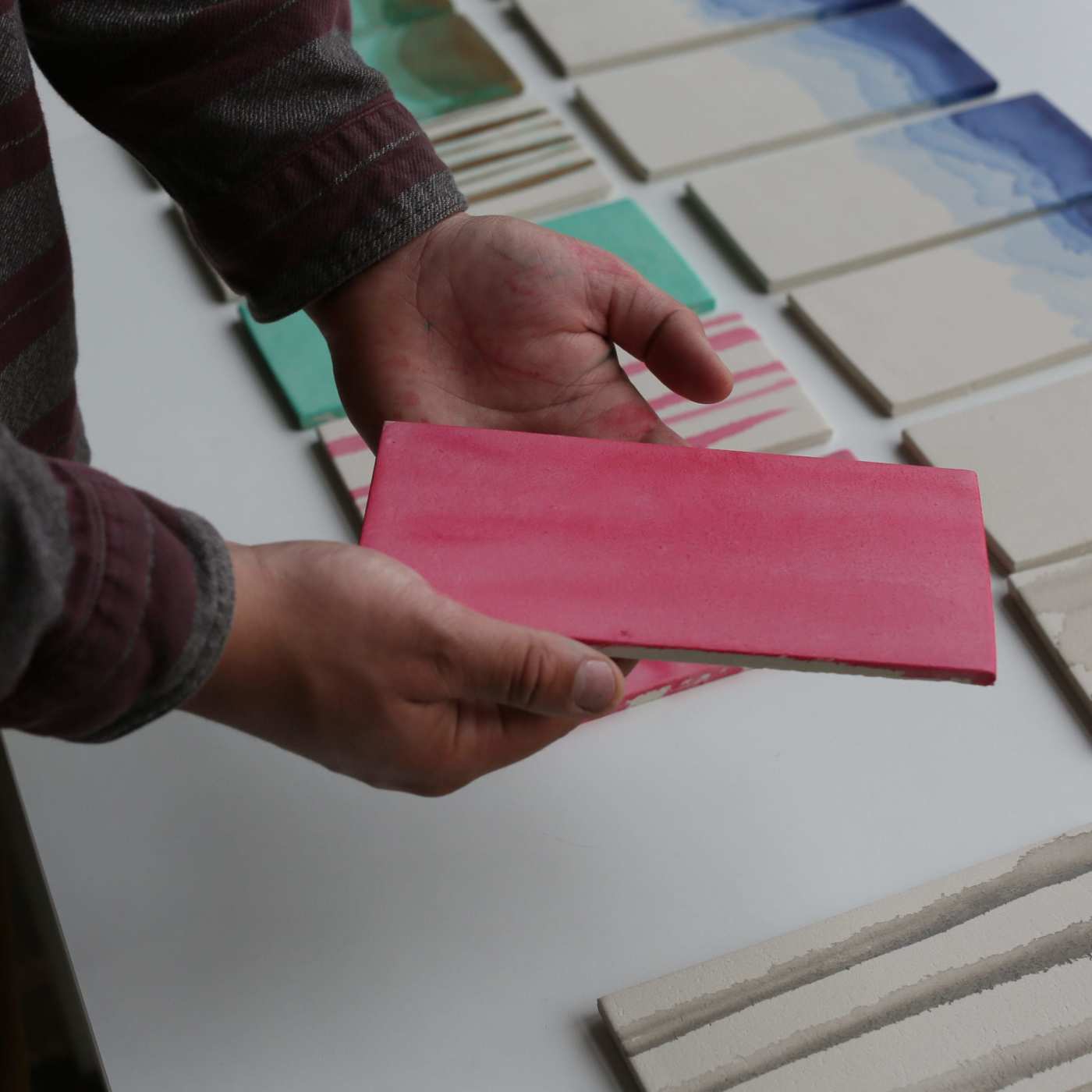 a person holding a pink tile over a table.