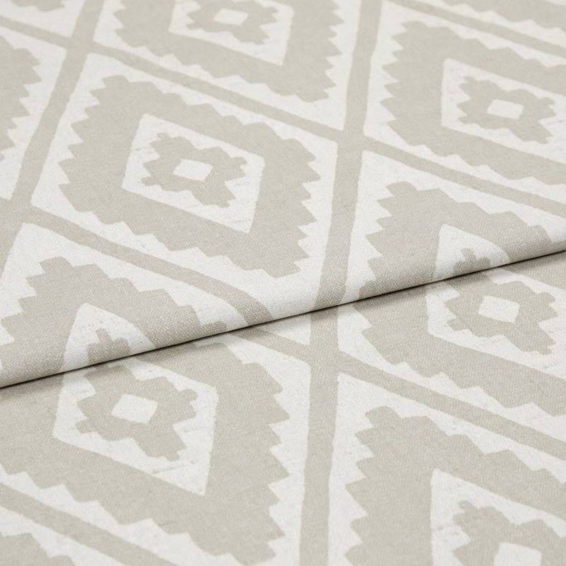 Folded woven upholstery fabric with beige-and-white diamond Aztec-style pattern, folded diagonally across the frame; crisp texture visible, photographed in soft, even studio lighting as a close-up.
