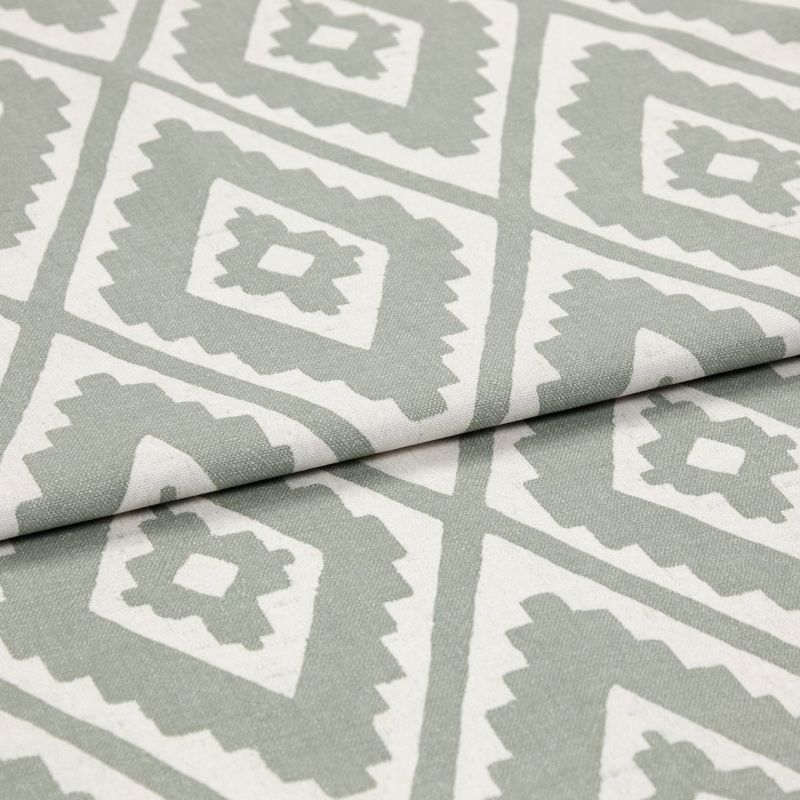 Folded woven fabric featuring repeating jagged-diamond, Aztec-like motif in sage green and off-white â€” layered across itself, lying flat in a soft, evenly lit close-up highlighting weave texture.
