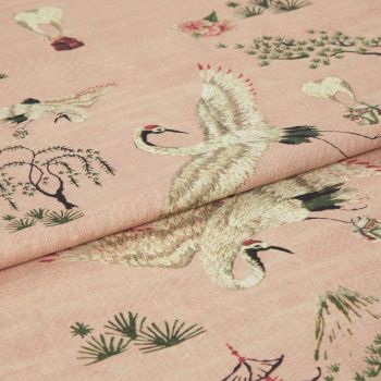 Pink woven fabric printed with red-crowned cranes and stylized trees â€” folded to show layered panels â€” close-up on a soft textile surface under soft, even lighting.