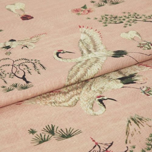 Pink woven fabric printed with red-crowned cranes and stylized trees — folded to show layered panels — close-up on a soft textile surface under soft, even lighting.