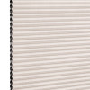 Beige pleated honeycomb cellular blind, fully lowered with visible black cells along the left edge; filtering light in a close-up studio view of the shade surface.