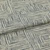 Woven upholstery fabric, cream base with gray, hand-drawn concentric-square pattern, folded over itself; photographed close-up under neutral studio lighting, showing textured weave and a layered edge.