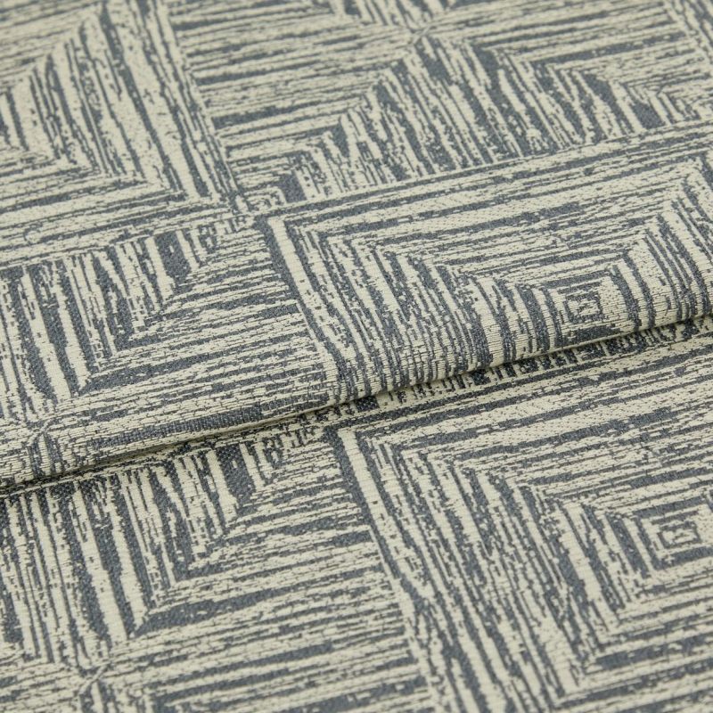 Woven upholstery fabric, cream base with gray, hand-drawn concentric-square pattern, folded over itself; photographed close-up under neutral studio lighting, showing textured weave and a layered edge.