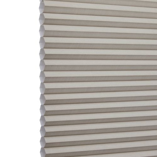 Cellular (honeycomb) window shade, beige pleated fabric hanging fully lowered with hexagonal cells, closed and gently filtering light; close-up interior view focusing on repeating horizontal folds.