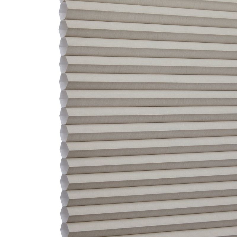 Cellular (honeycomb) window shade, beige pleated fabric hanging fully lowered with hexagonal cells, closed and gently filtering light; close-up interior view focusing on repeating horizontal folds.