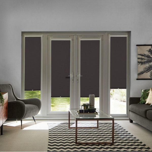 Dark roller blinds on four French door panes and sidelights, partially lowered blocking light with a gap revealing lawn, in a living room with sofas, glass table, chevron rug.