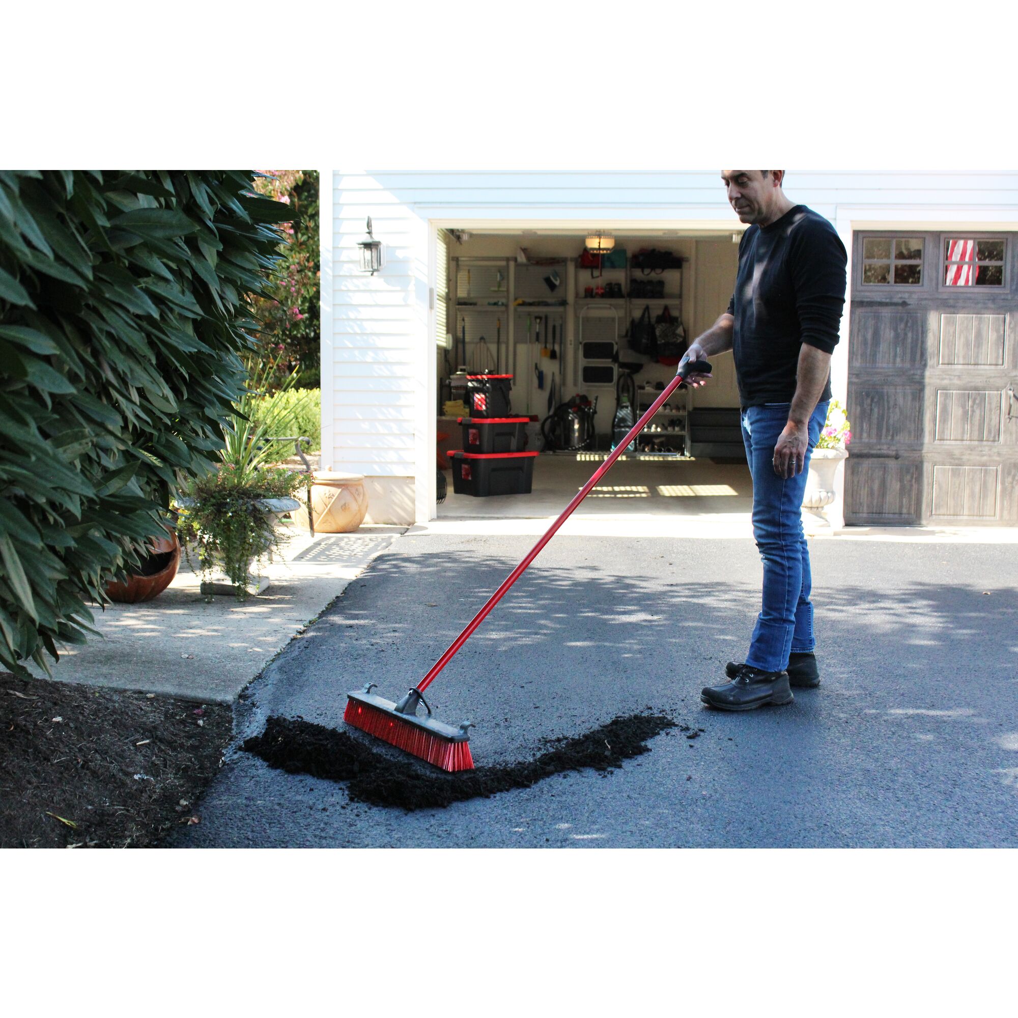 24 inch heavy duty push broom being used by a person to push dirt aside.