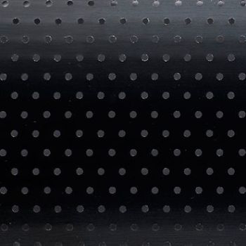 Black roller blind with regular small circular perforations — lowered and closed, the holes subtly admit faint light — set in a dim interior against a smooth background with a gentle top gradient.