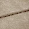 Beige textured fabric folded diagonally, overlapping along a soft crease â€” close-up of a chenille-like upholstery or curtain textile with subtle ribbed pile, even neutral lighting on a flat surface.