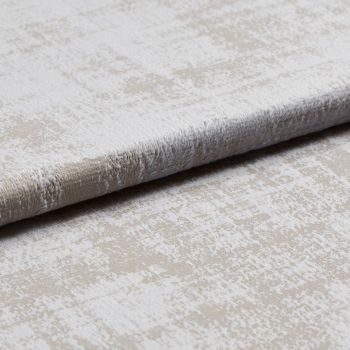 A folded plush velvet-like upholstery fabric with a mottled beige and off-white pattern is layered to reveal pile and edge, shown close-up on a neutral surface under soft studio lighting.