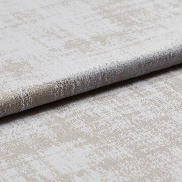 A folded plush velvet-like upholstery fabric with a mottled beige and off-white pattern is layered to reveal pile and edge, shown close-up on a neutral surface under soft studio lighting.