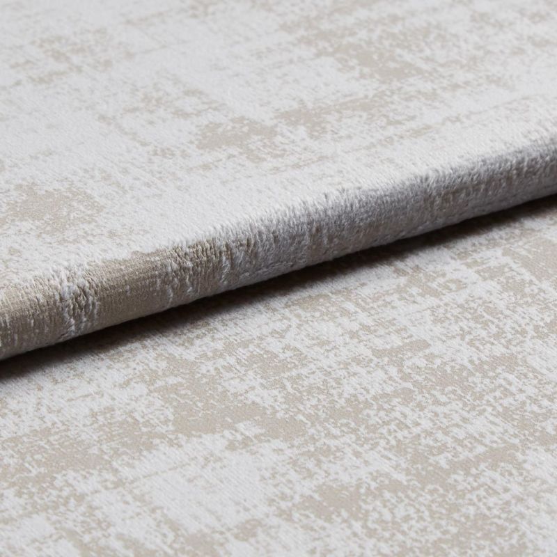 A folded plush velvet-like upholstery fabric with a mottled beige and off-white pattern is layered to reveal pile and edge, shown close-up on a neutral surface under soft studio lighting.