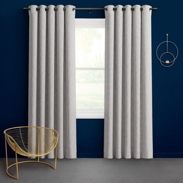 Grommet-top light gray curtains, hung on a black rod and parted to frame a bright window; modern navy-painted room with a gold wire chair and circular wall shelf.