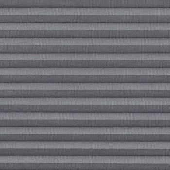 Gray pleated cellular blind, fully lowered with textured fabric forming horizontal ridges; blocking light and creating subtle shadow bands, shown in close-up interior view without visible window frame or exterior.