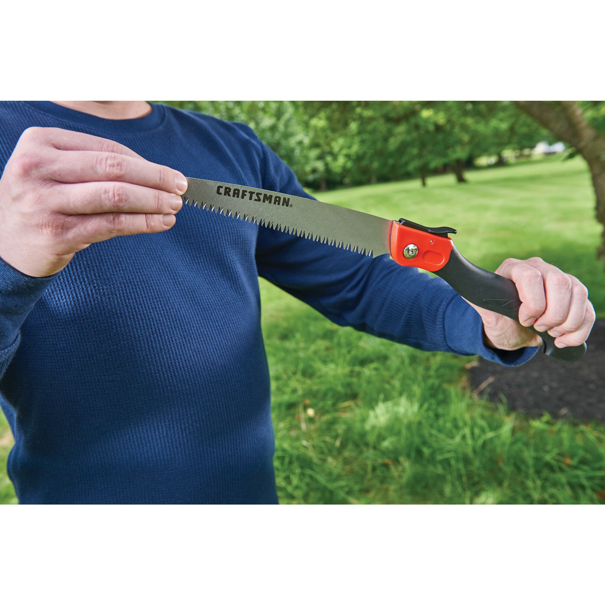 Folding saw being held by a person outdoors.