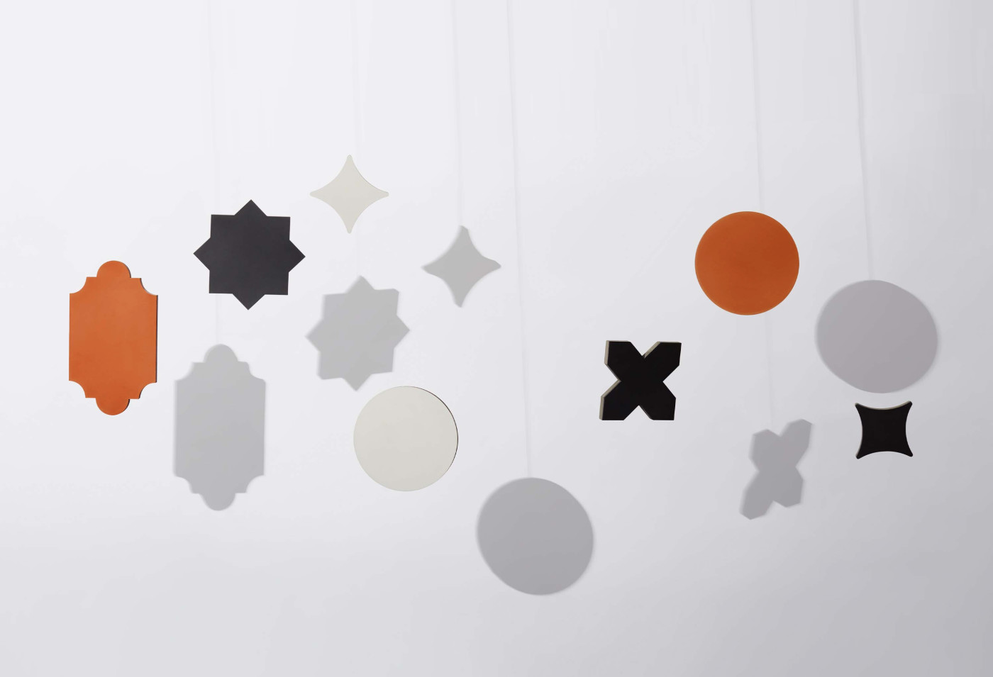 a group of different multi-colored shapes hanging from strings on a white wall.