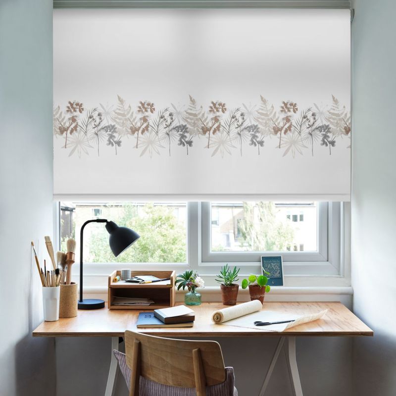 White roller blind with beige and gray botanical border, lowered across the window, filtering daylight. Above a wooden desk with lamp, potted plants, brushes and notebook in a bright home workspace.
British Herbs