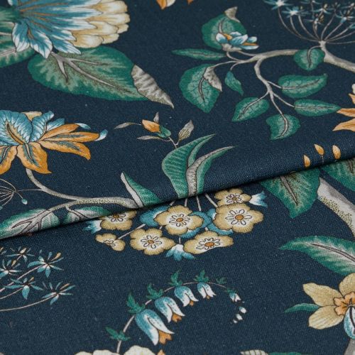 Folded dark teal fabric with botanical printâ€”green leaves and yellow, blue flowersâ€”folded along the center, overlapping to reveal textured weave; close-up on a flat surface under soft studio lighting.